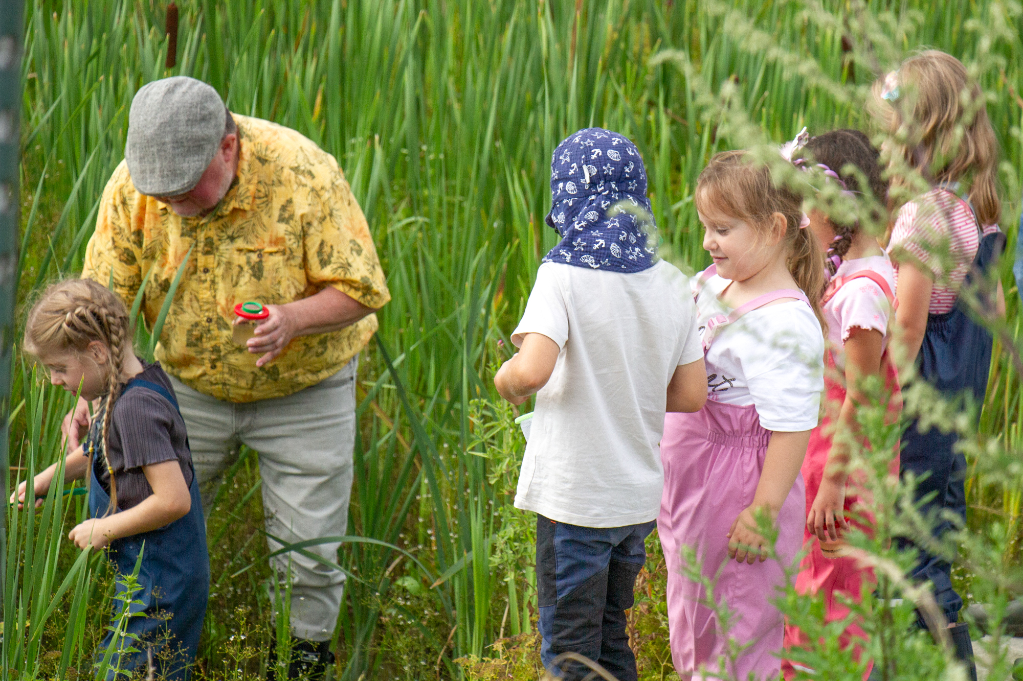 Rainer Oligmüller mit Luppenglas mit einer Gruppe von Kindern im Schilf