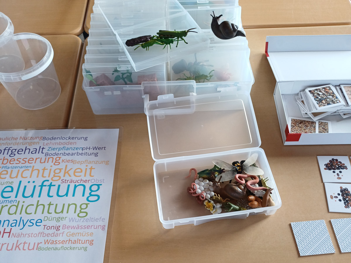 Lehrmaterial auf einem Tisch: Wordwolke, Tiermodelle, Karten des Bodenmemories