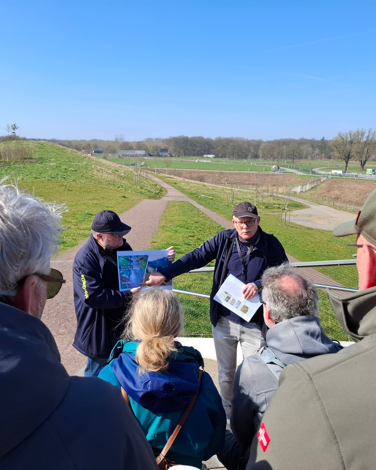 2 Emscherguides mit Gruppe zeigen einer Gruppe Grafik auf Papier im Wasser- und Erlebnispark Emscherland